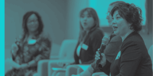 Photo of a woman holding a microphone, sitting with a diverse group of people, having a discussion